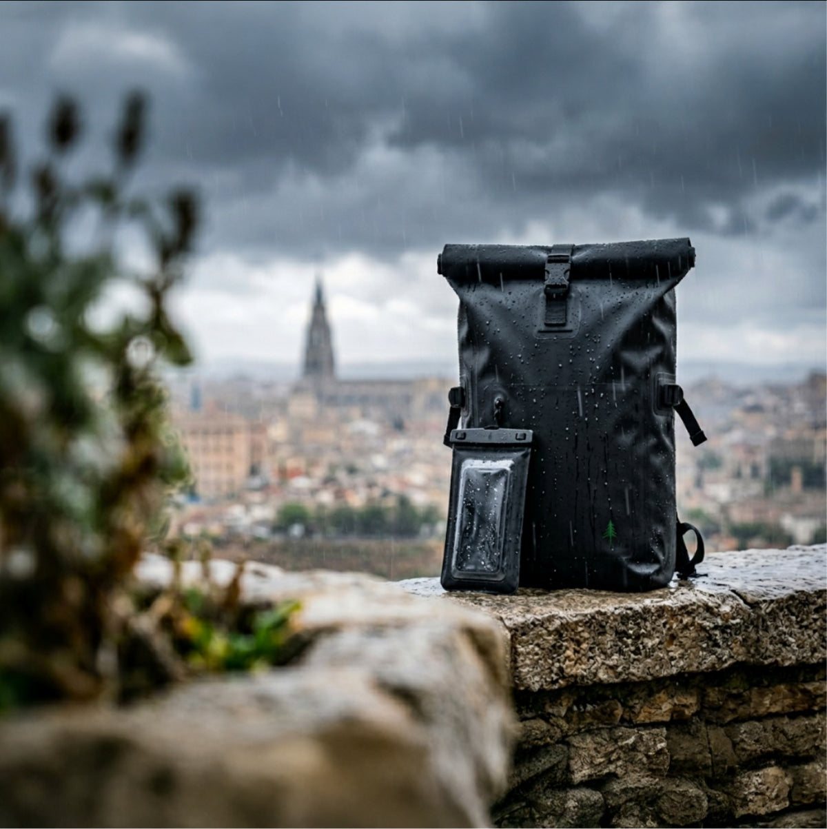 Produktfoto des Firona Dry Bundles im Regen: Die schwarze Firona Phone Pouch ist an einem nassen und wasserdichten Firona Waterproof Rucksack mit Roll-Top-Verschluss befestigt.