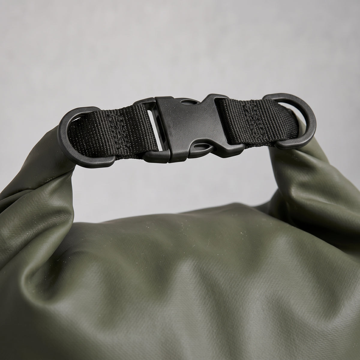 Nahaufnahme des geschlossenen Roll-Top-Klickverschlusses einer olivgrünen Dry Bag aus wasserdichtem Material mit schwarzem Gurtband vor hellem Studiohintergrund.