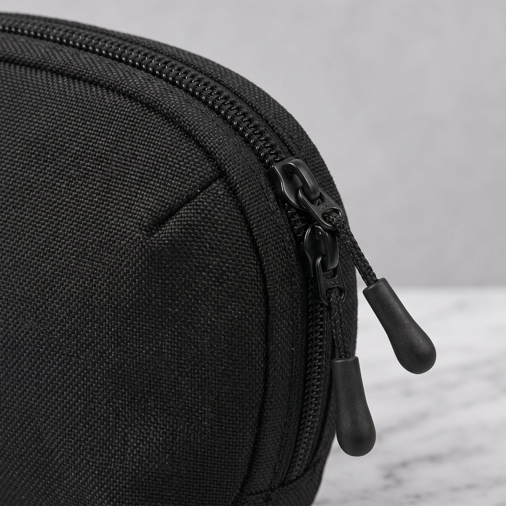 Nahaufnahme eines schwarzen Organizer Pouch aus robustem, strukturiertem Textilgewebe mit schwarzem Doppel-Reißverschluss und zwei Zipper-Anhängern, platziert ist die Aufbewahrungstasche auf hellem Untergrund in Marmoroptik.
