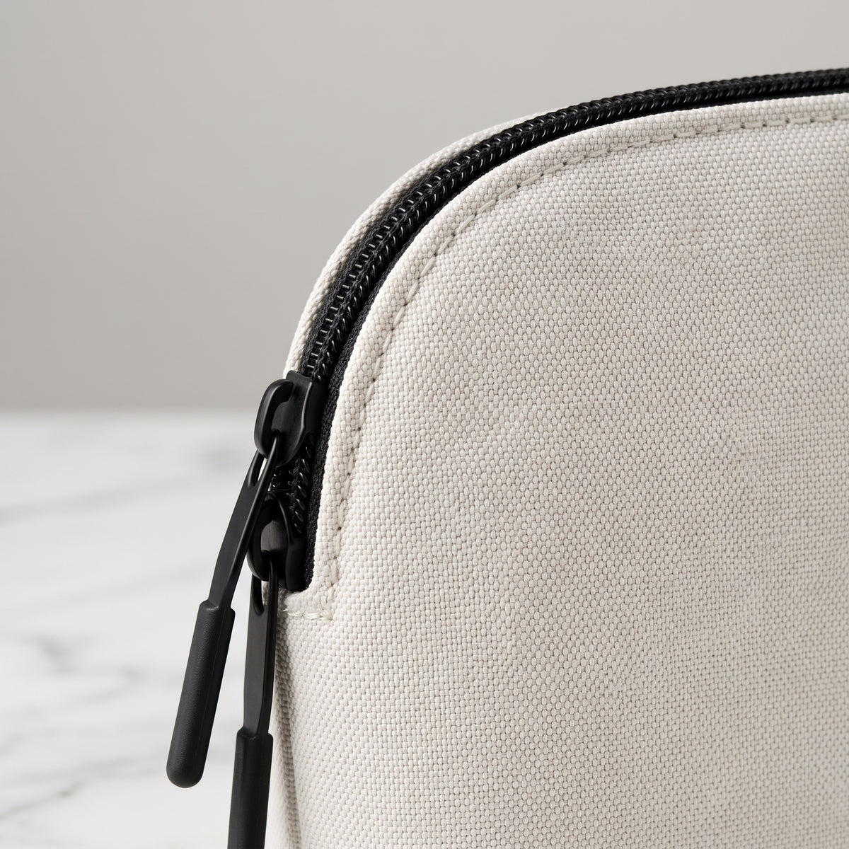 Nahaufnahme einer weißen Organizer Pouch aus robustem, strukturiertem Textilgewebe mit kontrastierendem, schwarzem Doppel-Reißverschluss und zwei Zipper-Anhängern, platziert auf einem hellen Untergrund in Marmoroptik.